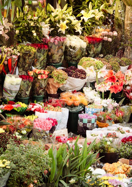 A vibrant display of fresh flowers at a florist shop, featuring a variety of floral arrangements including white lilies with large, open petals and green foliage, as well as bouquets wrapped in paper 