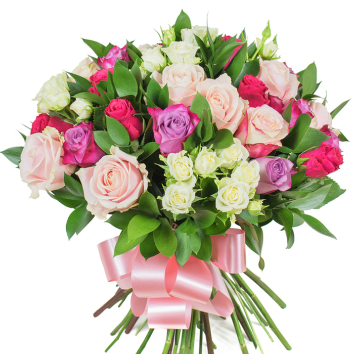 A luxuriant, rounded bouquet of mixed roses is artfully displayed against plain white, its dense grouping creating an abundant, tactile presence. The arrangement is dominated by generous, classic roses in pastel pink and creamy white, some fully unfurled to reveal soft, ruffled centers while others remain in poised bud form; brighter magenta or fuchsia roses interrupt the softness with vibrant punctuation, and slender lavender roses add a hint of cool, floral calm. Nestled among the larger blooms are clusters of small, pristine spray roses-primarily creamy white with subtle pale-yellow tones-that provide delicate texture and visual rhythm. Dark, glossy foliage-probably salal or ruscus-threads through the bouquet, its deep green leaves offering contrast and depth, and giving the composition a fresh, sculpted outline. The stems are gathered in a tight, professional tie and finished with a broad baby-pink satin ribbon knotted into an elegant bow whose shimmering loops cascade beneath the flowers, reinforcing the arrangement's celebratory character. Photographed in gentle, even lighting on a white background, every petal edge and leaf vein is visible, conveying freshness and meticulous florist craftsmanship. This bouquet conveys sentiments of love, appreciation, and celebration-ideal for anniversaries, Mother's Day, or a thoughtful birthday present for someone in Grove Park, Lewisham, or nearby Mottingham. The feel is polished yet intimate, a floral gift that balances softness and structure with an unmistakable sense of warmth and care.