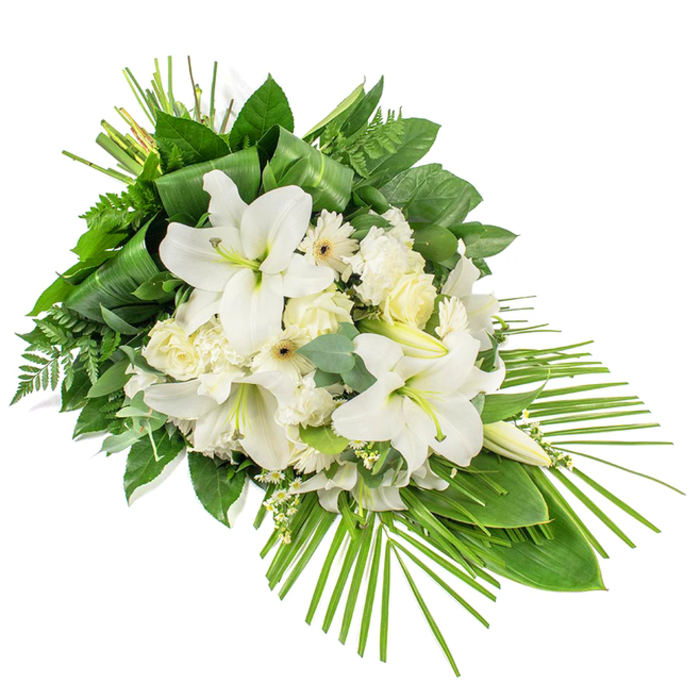 An elongated white and green funeral spray is set against a stark white background, its elegant lines suggesting it could rest along the front of a coffin or memorial table in a Grove Park service. The arrangement is designed in a one-sided, diagonal style, with the fullest cluster of blooms concentrated towards the upper left and gradually narrowing to a graceful point at the lower right. Dominating the centre are magnificent white Oriental lilies, their trumpet-like flowers fully open in places, with satin-smooth petals curving gently and revealing pale yellow-green stamens at their heart. Some lilies remain as slender buds, their presence hinting at continuing beauty. Nestled around them are clusters of creamy white roses and ruffled white carnations, the contrast between the smooth rose petals and the frilled carnation edges adding depth and softness. White Gerbera daisies, each with a discreet cream or yellow centre, bring a subtle, contemporary note, and tiny white filler blossoms weave through the design, softening the spaces between larger blooms. The floral display is supported by a rich base of greenery: glossy dark green leaves, light fern fronds that lend a feathery texture, and rounded eucalyptus leaves in muted blue-green tones, all combining to create a layered, natural backdrop. Towards the top, a few long, narrow leaves are carefully folded and grouped together, adding a modern, structured accent. From the lower right edge, slender palm fronds sweep outward and slightly upward, enhancing the spray's length and giving it a sense of graceful movement. The overall mood is calm, respectful, and quietly elegant, a thoughtful choice for funerals or memorial services throughout Grove Park and the nearby tree-lined avenues leading towards Chiswick and the Thames.
