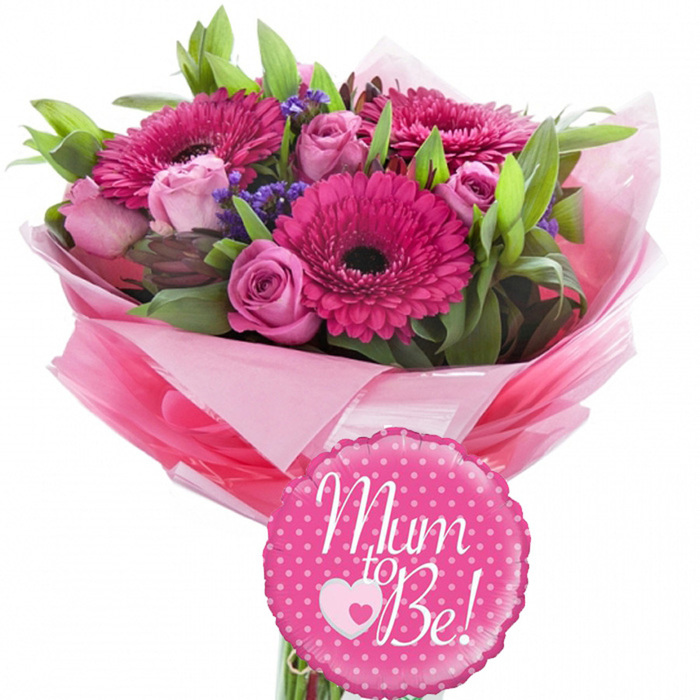 A celebratory maternity-themed bouquet is presented here with clarity and elegance, photographed against a white background that lets the arrangement's joyful colours take centre stage. Dominating the upper portion of the design, several large fuchsia pink gerbera daisies display their signature dark centres, each flower formed from numerous smooth petals that radiate outward in perfect symmetry, suggesting optimism and cheer. Interwoven with these bold blooms are softer, pastel pink roses, some still closed into neat, rounded buds and others opening into layered cups of petals, creating gentle curves and shadows that add depth and romance. Sprinkled amongst the main flowers, small purple filler blossoms mimic statice or limonium, their clustered, slightly textured heads introducing a cool, airy contrast to the pinks. Supporting the arrangement, lush green foliage fans out from the base and between the stems, with a mix of slender, arching leaves and broader greens that lend structure and a natural sense of abundance. The bouquet is hand-tied and wrapped in a generous collar of pink tissue paper, with different shades layered together so that lighter blush tones peek out behind slightly deeper pinks. This wrap is then enclosed in a protective sleeve of clear, glossy cellophane that subtly reflects the light and enhances the impression of a professionally prepared gift. Resting just in front of the wrapped stems, a round foil balloon in bright pink is decorated with crisp white polka dots and the joyful message Mum to Be! written in flowing white script, accompanied by a small heart motif. The combination of fresh flowers and playful balloon creates an uplifting tribute for an expectant mother, perfectly suited to baby showers and intimate celebrations across Grove Park, from riverside homes to quiet residential streets shaded by mature trees.