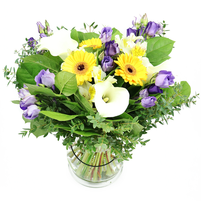Elegantly composed in a clear glass cylinder, this vibrant mixed bouquet stands against a pure white backdrop, inviting the eye to travel from the sun-bright yellow gerberas to the airy whiteness of calla lilies and the gentle violet of lisianthus. The daisies' dark centers draw you in, while the lisianthus clusters curl in soft ruffles, some fully opened, others poised as buds, creating a sense of motion within stillness. White alstroemeria with pale yellow streaks add a delicate texture, and the greenery-silvery eucalyptus and broad emerald leaves-frames the bouquet with a lush, garden-fresh weight. The stems are visible through the clear vase, bound by a slender black tie that keeps everything neatly aligned as water glistens around them. This is a bouquet of clarity and joy, a versatile gift that speaks of clean lines, modern grace, and quiet celebration. In Grove Park, it makes a refined centerpiece for a family gathering at home, a thoughtful gesture for a friend, or a bright welcome for a new workspace. Delivered fresh with reliable same-day dispatch across Grove Park and the surrounding SE London patch, it carries warmth and a touch of sophistication to any room.