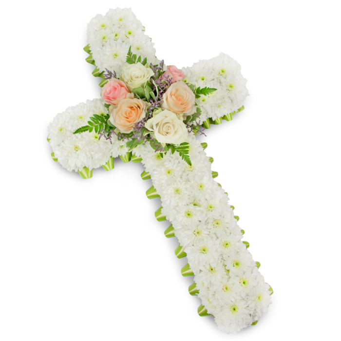 This photograph presents a solemn yet gently uplifting floral tribute in the shape of a Christian cross, isolated against a brilliant white background that enhances its lines and colours. The entire body of the cross is densely packed with white button chrysanthemums, each tiny flower nestled tightly beside its neighbour to form a deep, pillowed surface. The blooms create an even field of white, with subtle variations in texture that catch the light and give the impression of softness and quiet strength. At the point where the arms and stem of the cross intersect, a graceful bouquet of roses serves as the central focus. These roses open fully in harmonious shades of blush pink, creamy ivory, and mellow peach-apricot, their layered petals arranged in spirals that suggest affection, remembrance, and the warmth of shared memories. Around them, slender green fern leaves extend outward in gentle arcs, adding texture and a sense of natural movement, while delicate sprigs of pale lavender or lilac filler flowers weave through, bringing a fine tracery of colour to the design. The entire outline of the cross is neatly defined by a slim lime green ribbon that peeks from beneath the chrysanthemum petals, providing a contemporary edge and a crisp finish to this otherwise traditional form. The overall impression is peaceful and contemplative, ideal for a funeral or memorial ceremony in Grove Park, near the leafy paths and quiet roads that surround the area. Carefully crafted by local florists who understand the needs of grieving families, this floral cross stands as a visual expression of sympathy, faith, and enduring love.