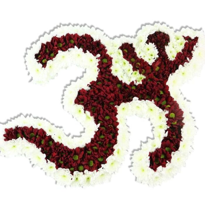 A meticulously sculpted floral Om (Aum) symbol sits prominently against a clean white background, its iconic contours articulated with dense masses of tiny, dark red to maroon chrysanthemum-like flowers. The arrangement recreates every element of the Sanskrit character - the rounded '3' form, the connected curving stroke that descends, and the crescent-and-dot motif above - with careful attention to proportion and line. Each small maroon bloom shows a pale lime-green centre, a subtle natural accent that adds depth and lively variation across the darker field. Surrounding and defining the symbol is a generous, undulating border of pristine white spray chrysanthemums; their soft, ruffled petals trace the outer edges and the interior negative shapes, producing a crisp contrast that makes the Om read clearly from a distance. The piece has a compact, plush texture: petals packed closely produce a velvety plane that appears cool and softly cushioned to the touch, while a faint drop shadow beneath gives a reassuring sense of physical presence and weight. Bathed in gentle studio light the colours remain rich and contemplative - the deep maroon suggesting solemnity and resonance, the white border lending clarity and peace. This composition is well suited to spiritual gatherings, memorial services, or yoga and meditation events in Grove Park and neighboring Lewisham venues; it speaks of reverence, careful craftsmanship, and the quiet dignity of handcrafted floral tributes, and can be prepared for local delivery across Grove Park, Baring Road and around Grove Park Nature Reserve.