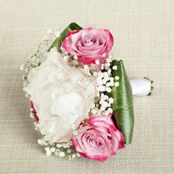 Rich with the gentle charm that characterises Grove Park, this expertly crafted bouquet lies atop a pale, textured fabric much like the table linens at a local gathering. At its heart, two showstopping pink roses make a statement with petals brushed in hues of fuchsia and soft blush, spiralling inwards to tightly furled, fragrant centres. Poised between them, a lush white peony unfolds in all its ruffled glory-each petal layered atop the next, building a vision of fullness and pure romance. Wispy clouds of baby's breath, or Gypsophila, are artfully scattered among the larger blooms, contributing both lightness and a touch of whimsical magic, reminiscent of an early morning stroll along Grove Park's tranquil roads. Wide, deep green leaves, likely aspidistra or ti, encircle the bouquet with their bold structure and subtle gloss, emphasizing the lively contrast of bridal white and celebratory pink. Each stem is bound with a smooth wrap of pristine white satin ribbon that gently trails towards the edge, ready to be clasped for a wedding or special event in the local community. Flooded with soft, even light, the composition's blend of colour, natural shape, and scent creates a moment of shared anticipation and happiness-perfect for Grove Park's bridesmaids or anyone wishing to celebrate a significant occasion with fresh local blooms and thoughtful design.