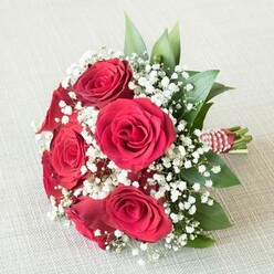 Laid gently upon a pale, textured linen that echoes the light simplicity of Grove Park mornings, this artisanal bouquet is an ode to refined romance. At its centre, a cluster of rich red roses blooms vibrantly, each velvety petal curling outward in a timeless spiral, suggesting both classic passion and contemporary elegance. The roses' bold presence is tempered by a generous sprinkling of soft white baby's breath, whose delicate, cloud-like formations suggest a touch of early mist rising above the Thames nearby. Fresh leafy greens-including bright ruscus-punctuate the bouquet, their lively hues and polished surfaces mirroring the natural beauty found along Grove Park's tree-lined roads. The bouquet is tied securely at the base with a red-and-white striped ribbon, adorned with a spiralling accent of lustrous white pearls, a small but significant flourish that evokes the craftsmanship and care characteristic of Grove Park Florist. Bathed in soft, even light, every flower and leaf appears freshly gathered, the arrangement embodying warmth, heartfelt sentiment, and graceful celebration. Perfect for romantic gestures, bridal moments, or thoughtful tokens for loved ones across Grove Park, this display blends tradition with the spirit of contemporary floristry, offering a visual and emotional experience that lingers in memory long after the last petal has fallen.