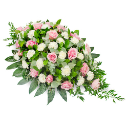 This elongated funeral spray, presented on a clean white background, forms an elegant teardrop silhouette that naturally draws the gaze from its broad, rounded head to its slender, tapering end. At the heart of the design are numerous pastel pink roses, their petals unfolding in soft spirals. Some blooms are fully open, revealing intricate layers, while others remain partly closed, adding depth and variety. Between them, white carnations are tucked carefully, their ruffled petals lending a billowy, cloud-like feel that softens the overall look. The flowers rest on a bed of deep, glossy green leaves that curve outward, providing a defined, structured base that frames the spray with quiet strength. Interwoven with this darker foliage, silvery-green eucalyptus leaves offer a muted, calming tone and a suggestion of fresh, aromatic greenness. From the fine, pointed tip of the arrangement, slender stems of trailing greenery extend gracefully, echoing the gentle fall of leaves you might see along the paths and green spaces around Grove Park. The colour palette is restrained yet emotive: tender pinks and pure whites balanced by natural greens, conveying solace, peace, and affection. This is a classic casket spray or front-facing tribute, the type a local family might place beside a photo or on a coffin during a farewell service. The arrangement feels composed and respectful, crafted with the kind of sensitivity and steady hand that comes from years of arranging sympathy flowers for the Grove Park community.