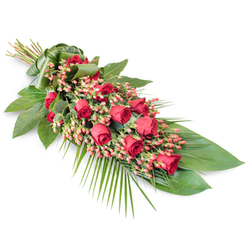 An elongated sympathy spray filled with deep red roses is set against a pristine white backdrop, the clean negative space allowing every detail of the floristry to be appreciated. The spray is arranged diagonally, with the stem ends gathered at the top left and the floral body flowing toward the bottom right in a soft, tapering line. Along this line, velvety red roses are arranged in overlapping clusters, some buds still tight and full of potential, others half-open or fully blooming, lending the piece a sense of gentle progression and life. Between the roses, dense clumps of pinkish-red Hypericum berries are tucked carefully, each rounded berry catching tiny flecks of light and introducing a slightly brighter note to the red palette. Surrounding this central feature, a rich variety of foliage provides structure and depth: broad, polished dark green leaves cradle the roses, while fine, feathery palm fronds reach outward, softening the edges and reinforcing the elongated, sheaf-like shape. Subtle stems of additional greenery, reminiscent of garden foliage, appear throughout, giving the tribute a natural, slightly garden-like character despite its formal composition. The stems are wrapped in a wide strip of green leaf at the upper left, creating a smooth, natural cuff instead of a traditional ribbon. This thoughtful detail, typical of arrangements hand-crafted by Grove Park Florist for services around Grove Park, Chiswick, and the surrounding churches, enhances the sense of care and craftsmanship. The resulting tribute feels both traditional and slightly contemporary, offering a calm, heartfelt way to honour a loved one's memory during funerals, memorials, or quiet family goodbyes.