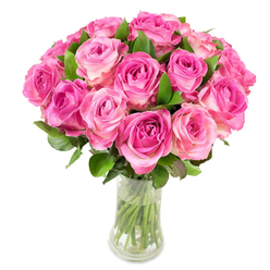 A full, rounded bouquet of roughly two dozen fresh pink roses creates an immediate sense of joyful abundance; each bloom shows a colour gradient from intense magenta in its tightly furled centre to soft, almost pearly pink at the outer petals. The roses are arranged so closely they form a plush dome, green leaves peeking like secretive accents to emphasise the blossom tones and add depth. The clear glass vase-slender in the middle and curving at top and base-reveals cut stems plunged into clean water, a small, honest detail that speaks to freshness and care. Under steady, bright lighting, each petal's velvety surface catches light and shadow, and you can almost feel the softness beneath your fingertips or scent the lightly sweet, green-tinged fragrance of summer roses. This arrangement reads as a gesture of sincere affection-suitable for birthdays, anniversaries, or an unspoken I'm thinking of you. As someone who arranges for families in Grove Park and nearby Lee and Hither Green, I picture this bouquet delivered from local hands, crossing the footbridge by Grove Park Nature Reserve to bring a moment of beauty into a kitchen table, a hospital room, or a bedside on a lazy Sunday. It's a modern classic: confident, heartfelt, and quietly luxurious without ever feeling excessive.