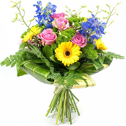 This elegant mixed bouquet is photographed upright against a white background, its colours and shapes echoing the relaxed charm of Grove Park's tree-lined streets. In the heart of the arrangement, soft pink roses bloom fully, their layered petals forming generous cups that suggest tenderness and heartfelt sentiment. Nestled close by are round, sunny yellow gerbera daisies, each centred with a deep brown eye, providing a striking contrast and a burst of warmth that immediately draws the gaze. Above the central cluster rise tall stems of vivid blue delphinium, their many small, bell-like florets aligned along slender stalks, injecting cool, calming tones and creating graceful height, much like the tall trees along the nearby riverside. The bouquet is enriched with abundant greenery: light, feathery fern fronds trail softly from the edges, while larger, smooth, dark green leaves, some subtly striped in paler tones, are wrapped in a careful band around the lower part of the bloom heads, shaping a structured collar that supports the arrangement. Throughout the flowers, bright green textured filler greens add soft, cushion-like volume and a fresh garden texture, filling any gaps and making the bouquet appear full and generous. Delicate, pale green stems tipped with small unopened buds extend from the top, giving a sense of life and ongoing growth. Beneath, the flower stems are neatly aligned and firmly tied, the natural-looking binding left visible to highlight the hand-tied craftsmanship that a local Grove Park florist would be proud of. The bouquet radiates joy and optimism, ideal for marking anniversaries, congratulations, or simply bringing a touch of colour to a home near Chiswick or the surrounding area.