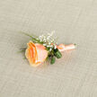 In the gentle morning light this peach rose boutonniere radiates an understated elegance that reads as both deliberate and effortlessly romantic. The single rose displays a rich, golden-apricot centre that graduates outward to a softer peach rim, its layered petals forming a plush, velvety cup that seems almost touchable. Sprigs of gypsophila punctuate the arrangement with tiny, cloud-like blossoms, their clean white points brightening the composition and lending an airy, whimsical character. Broad, glossy leaves encircle the base in soft loops, bringing a fresh, verdant contrast that grounds the piece while a slender fern adds a refined, textural accent. The stem has been expertly bound in matching peach satin, the ribbon tied neatly so its gentle sheen catches glimpses of light without overwhelming the bloom. There is a delicate, spring-like scent suggested when you imagine bringing it close - a faint sweetness that conjures orchard walks and early-season gardens. As a florist familiar with Grove Park and its neighbouring green spaces like Chinbrook Meadows and the local community halls, I picture this boutonniere being pinned on before a small ceremony or a summer reception; it is suited to intimate weddings and milestone moments. Crafted with the care customers expect from a local atelier, it pairs beautifully with muted suiting and pastel palettes, designed to photograph softly and endure through embraces and laughter. For couples planning a day in Grove Park or nearby, this piece feels like a tender, timeless choice - quietly stylish, thoughtfully made, and full of gentle emotion by Grove Park Florist.
