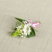 This delicate corsage-style boutonniere rests on a pale oatmeal, linen-like fabric, its neutral backdrop reminiscent of a sunlit table in a Grove Park townhouse. The central flower is a white alstroemeria-type bloom, open and luminous, its petals smooth and slightly curved, with subtle reddish-brown striping along the inner surfaces that gives it character without overpowering the design. Around it, several smaller white buds and partially opened blossoms nestle closely, evoking the gentle promise of flowers just beginning to unfurl. Sprigs of fine white baby's breath weave through the composition, adding a light, cloud-like texture that softens and romanticises the whole piece. On one side, a vivid bright green, cone-shaped cluster of tightly packed buds stands out, serving as a sculptural counterpoint to the softer petals and recalling fresh growth from nearby Chiswick's riverside gardens. Lush, broad dark green leaves frame the arrangement from beneath, while slender strands of arching grass-like foliage extend outward, giving a sense of motion and natural grace. At the base, the stems are wrapped neatly in a glossy pink satin ribbon, tied into a petite bow whose gentle sheen suggests celebration-perfect for a local wedding ceremony, prom, or anniversary dinner in Grove Park. The lighting is soft and even, bringing out the intricate veining in the petals and the gentle sheen of the leaves and ribbon. The boutonniere feels intentionally designed and lovingly assembled, a compact yet expressive floral accessory meant to be worn close to the heart on an important day.