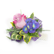 A compact, exquisitely crafted corsage or boutonnière set against a pristine white backdrop, the kind of small luxury you might tuck into a wedding lapel or wear at prom. At its heart sits a single partially open rose whose petals graduate from a soft, lavender-pink centre to a vivid fuchsia rim, the velvety layers catching a gentle studio light so the colour seems to glow from within. Nestled to the right of the rose is a tight cluster of indigo-purple florets-reminiscent of hydrangea or small sprays of delphinium-each tiny bloom punctuated by bright blue and lime-yellow-green centres that vibrate against the rose's softness. Surrounding the focal blooms is an artful mix of foliage: broad variegated ivy leaves with deep emerald cores and sunny yellow margins, silvery-green, slightly fuzzy leaves that read like lavender foliage, and slender asparagus-fern tendrils that thread through the composition to give it air and movement. A sculptural curled leaf striped in green and cream adds a modern graphic note, its curve echoing the rose's spiral. The whole arrangement is set on a layer of dark purple, web-like mesh that peeks out beneath the flowers and creates shadowed depth and a contemporary edge. To the lower right, a short strand of luminous white pearls suggests a wristlet or decorative pin and lends old-world elegance. The overall impression is romantic yet contemporary, tactile in texture and balanced in colour-an heirloom-ready small piece designed for ceremonies, evening celebrations, or quiet milestone moments, made to be both seen and gently held.