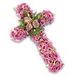 This image shows a graceful floral cross arranged against a crisp white background, the contrast making every petal stand out. The cross is generously covered with flowers in shades of pink, mauve, and soft purple, layered so densely that the piece looks plush and comforting, like a bed of blossoms laid gently in remembrance. At the central point where the arms meet, three open roses in a soft dusty rose and light mauve tone provide a clear focal point. Their petals are full and gently spiralled, creating the sense of a tender heart at the centre of the tribute, echoing the love shared at many quiet goodbyes in Grove Park. Around these roses, slim fern fronds and bright green leaves weave between the larger blooms, injecting vibrant colour and a natural, garden-inspired touch that feels in tune with the area's leafy character.
From this centre, the arms and base of the cross are entirely filled with trumpet-shaped Lisianthus flowers. They appear in a spectrum of pinks and mauves, some paler, others richer, with a number showing darker centres that add delicate depth. Between them nestle fine filler flowers in pale pink, cream, and soft lavender, while scattered light green buds provide a gentle hint of new life and hope. Just at the outer edges, discreet glimpses of a darker purple ribbon or supporting base peek through, shaping the cross and giving it a subtle sense of structure without detracting from the floral abundance. The overall mood is peaceful and reverent, like a carefully considered farewell created by Grove Park Florist for a funeral, memorial service, or graveside tribute, expressing faith, respect, and enduring remembrance through colour, texture, and form.