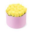 A pastel pink cylindrical flower box, brimming with yellow roses, stands alone in front of a spotless white backdrop, the entire composition exuding quiet luxury and joy. The hatbox has a soft, matte finish reminiscent of velvet or suede, its muted blush tone offering an elegant contrast to the vivid blooms gathered above. Inside, around two dozen fresh yellow roses are meticulously arranged into a smooth, rounded dome that extends just beyond the rim of the box, creating a sense of fullness and abundance. Each rose is in perfect condition, with velvety petals unfurling in classic spiral formations, transitioning from gentle golden-centre tones to brighter, lemony edges that catch the light. Here and there, a sliver of green foliage appears between the blooms, keeping the arrangement feeling fresh and natural without disrupting its clean lines. The even lighting and white background ensure that the interplay of yellow and pink remains the focal point, much like a carefully curated product image you might see when ordering flowers for delivery to Grove Park, Strand-on-the-Green, or nearby residential streets. The mood is upbeat yet refined, suggesting a gift well suited to birthdays, anniversaries, Mother's Day, or simply sending a thoughtful gesture of friendship to someone along the leafy roads between Grove Park and Chiswick. The design feels like something a skilled Grove Park florist would craft to bring a burst of sunshine indoors, brightening a windowsill, dining table, or home office with its cheerful colour palette and polished presentation.