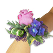 A single wrist corsage rests diagonally on a fair-skinned forearm against a clean white backdrop, a study in modern romanticism and quiet celebration. At its heart a velvety lavender-pink rose unfurls in a generous, partially open bloom, each petal catching a faint, dewy sheen that suggests freshly cut blooms from an early summer garden. Nestled close are saturated clusters of indigo-blue hydrangea, their tiny florets glowing with pale blue centres that set off the rose's soft blush and add luminous depth. Variegated ivy leaves frame the composition-dark green centres rimmed in cream and yellow-bringing a classic, almost heirloom touch, while slender silvery-green sprigs, reminiscent of eucalyptus, lift the silhouette with soft, feathery texture. A broad leaf, boldly striped in white and green, is curled into a sculptural spiral that introduces a contemporary flourish and a glossy contrast to the matte petals. Beneath and around the flowers, an open-weave deep purple mesh peeks through, its lacy texture amplifying the hydrangeas' tones and lending a faint, evening-like sparkle as though catching light from nearby jewellery. The overall scent would be cool and slightly herbal, the surfaces alternating between silky rose petals, crisp ivy, and smooth glossy foliage. Composed with the assurance of an experienced florist, this corsage feels both celebratory and intimate-perfect for a prom, bridesmaid, or anniversary evening in Grove Park or nearby Hither Green-an accessory designed to be seen, touched, and remembered.